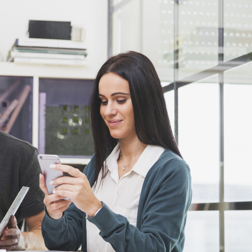 cheerful-young-woman-using-phone-office